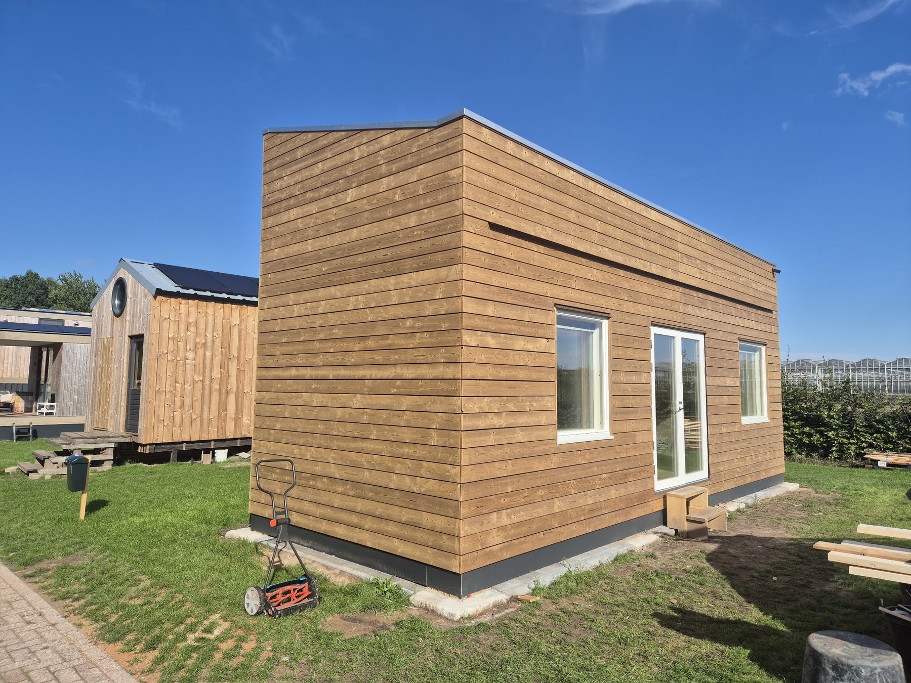 Een nieuw gebouw met horizontale houten gevelbekleding en witte kozijnen op een grasveld
