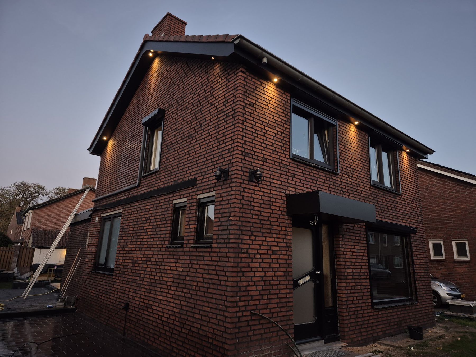 Een bakstenen woning in de schemering met nieuwe donkere boeidelen en brandende spotjes in het overstek