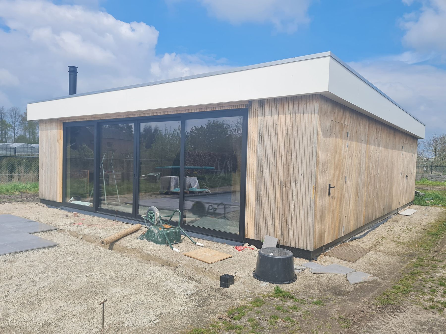 Een nieuwe houten aanbouw met witte daklijst en een grote zwarte glazen schuifpui